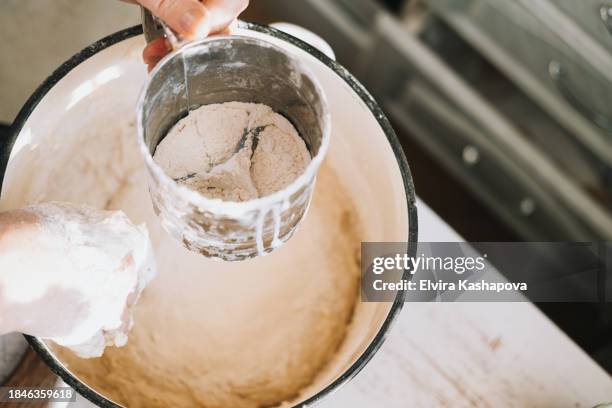 grind the flour in an iron calico mug over the pan with the dough. atmospheric photo of homemade baking, top view - sifting stock pictures, royalty-free photos & images