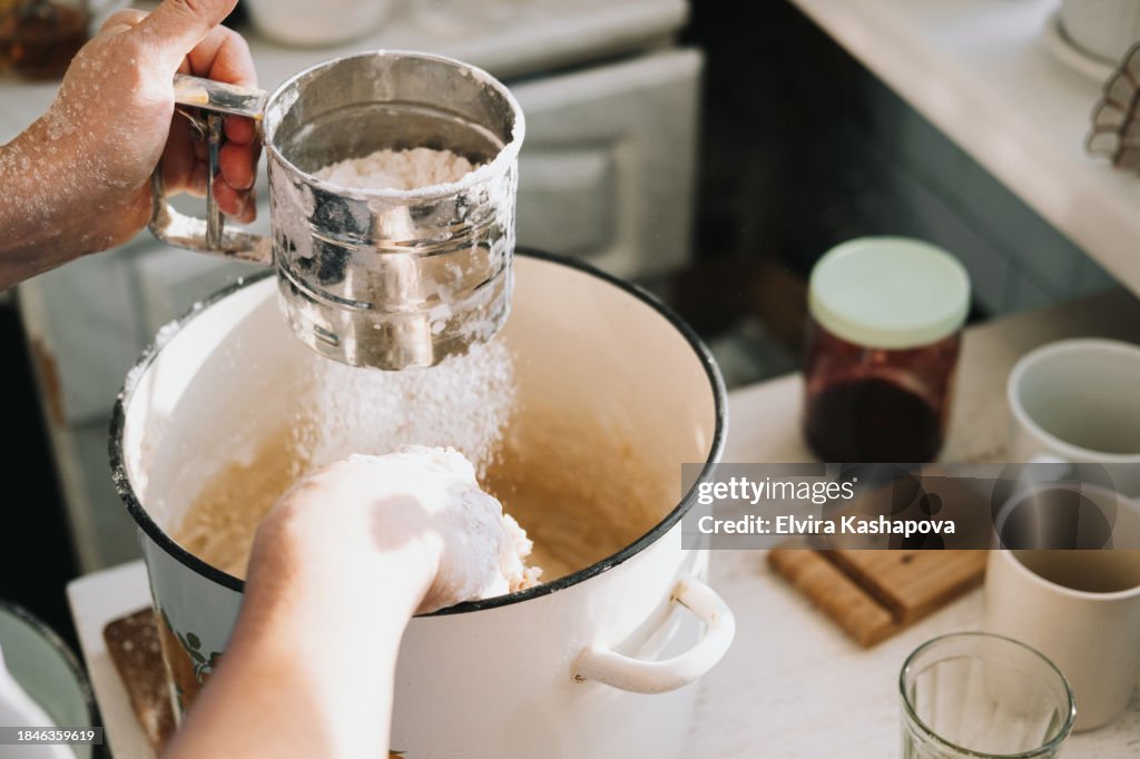Grind the flour in an iron calico mug over a baking sheet with dough. Atmospheric photo of homemade baked goods on the kitchen table