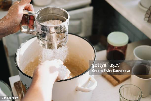 grind the flour in an iron calico mug over a baking sheet with dough. atmospheric photo of homemade baked goods on the kitchen table - sifting stock pictures, royalty-free photos & images