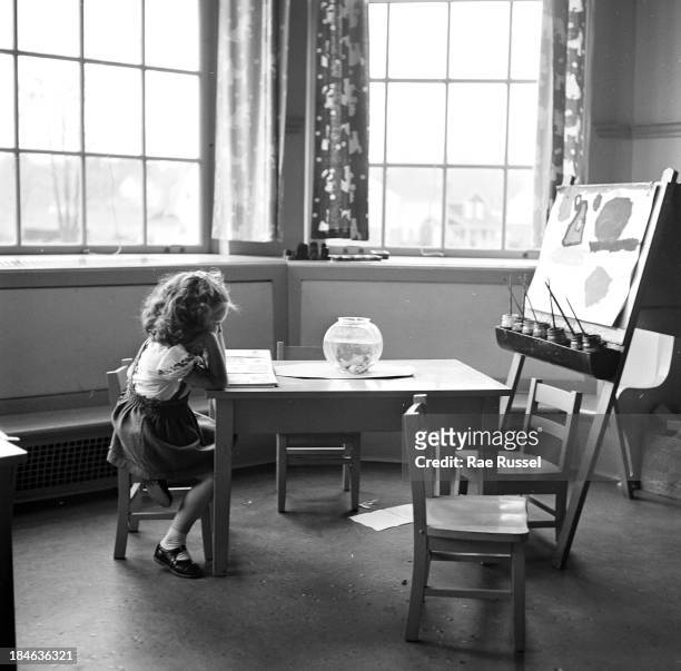 On her first day of nursery school, a young girl sits at a table and reads a book, her head in her hands, Madison, New Jersey, 1948. The picture was...