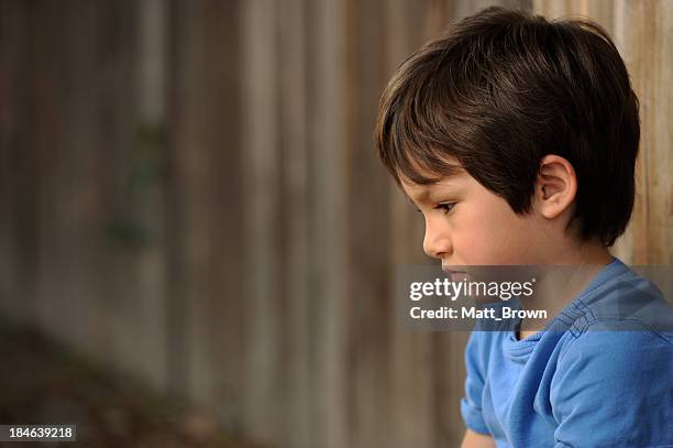 lonely boy in a blue shirt sits against a wooden fence - one boy only stock pictures, royalty-free photos & images
