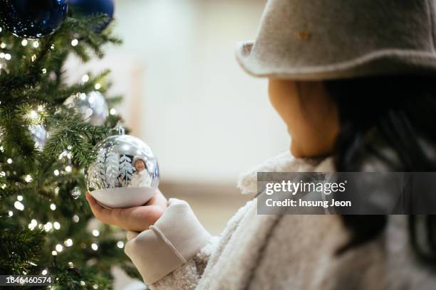 little girl holding a silver christmas ornament with a christmas tree in the background - like a child in a sweet shop stock pictures, royalty-free photos & images