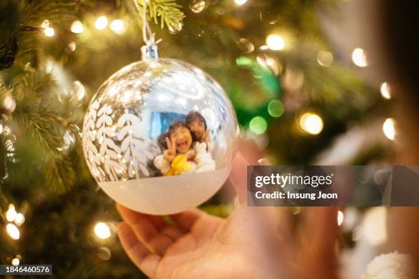 little girl holding a silver christmas ornament with a christmas tree in the background - like a child in a sweet shop stock pictures, royalty-free photos & images
