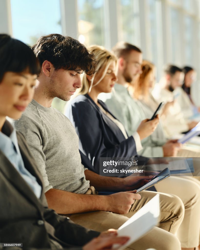 Young businessman reading his CV while waiting for job interview with other candidates.