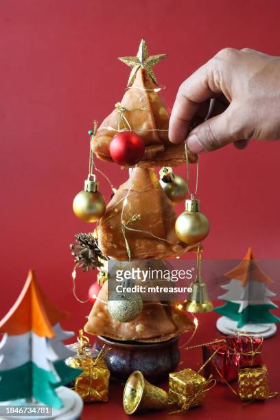 close-up image of unrecognisable person hanging red and gold baubles, christmas tree designed from batch of fried samosas, ramekin of mint coriander dip trunk, gold star, wooden christmas trees painted like national flag of india (tricolour), mini present - india flag stock pictures, royalty-free photos & images