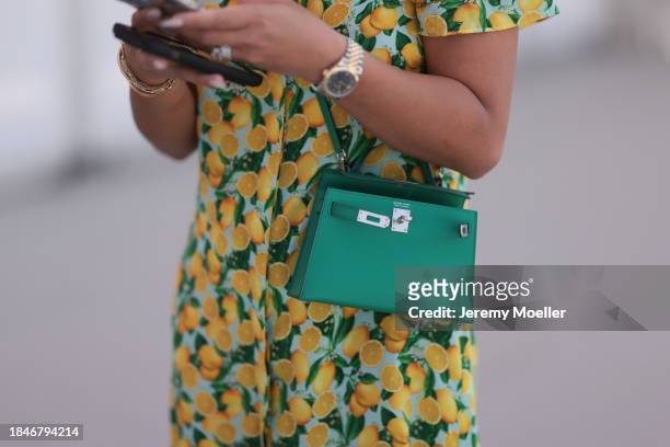 Lou Anne Falsis seen wearing yellow / green lemonade print pattern short dress, Hermès Kelly green leather mini bag, silver / gold watch, silver /...