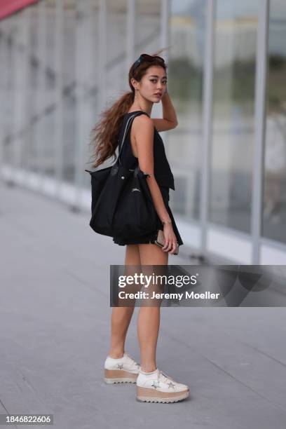 Elle Chen seen wearing Prada black sunglasses, gold earrings and necklace, black pinstripe suit gilet, matching black checked belted pleated short...