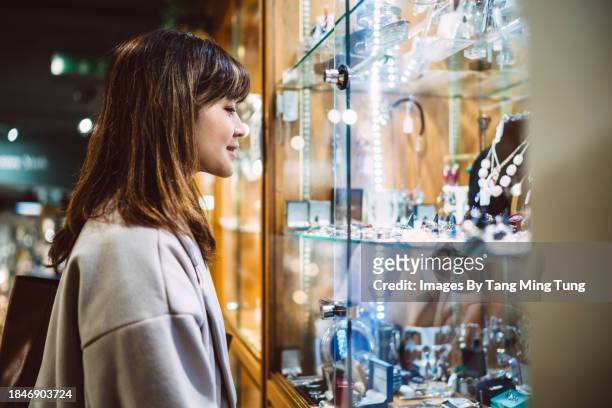 beautiful asian woman looking at jewellery through a glass display cabinet in a jewellery shop - kaufsucht stock-fotos und bilder