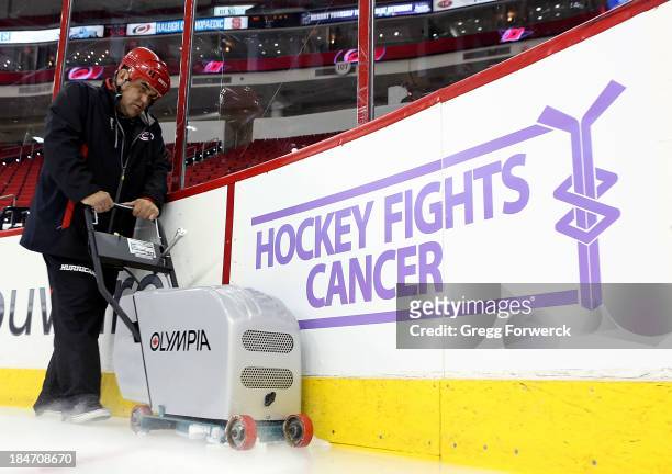 Member of the Carolina Hurricanes ice crew cleans the ice in front of a Hockey Fights Cancer dasher board prior to an NHL game against the Chicago...