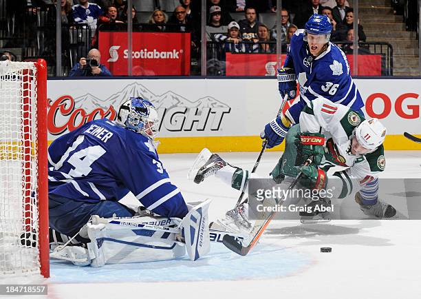 James Reimer of the Toronto Maple Leafs defends the goal as teammate Carl Gunnarsson battles with Zach Parise of the Minnesota Wild during NHL game...