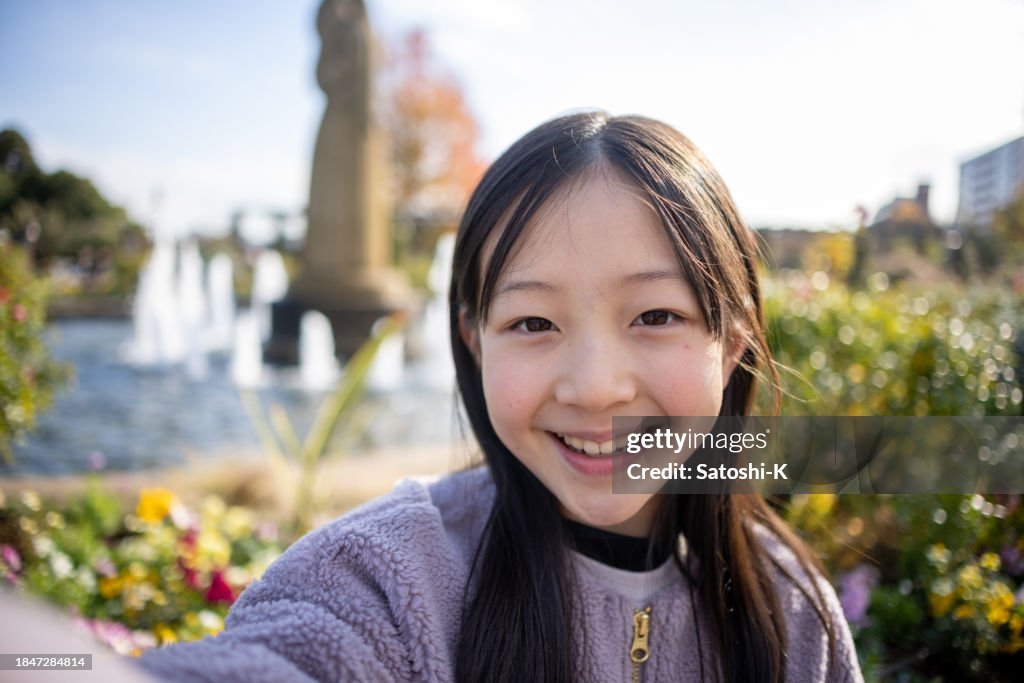 Teenage girl taking selfie picture in public park - looking at camera