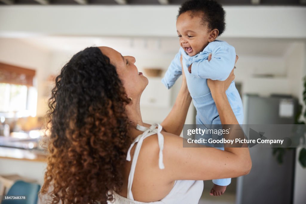Smiling mom standing with her baby boy in har arms at home