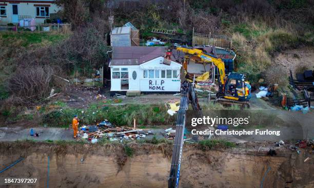 In this aerial view a beach chalet adorned with 'RIP HOME' is demolished by workers before it falls down the sea cliff on The Marrams at Hemsby Beach...