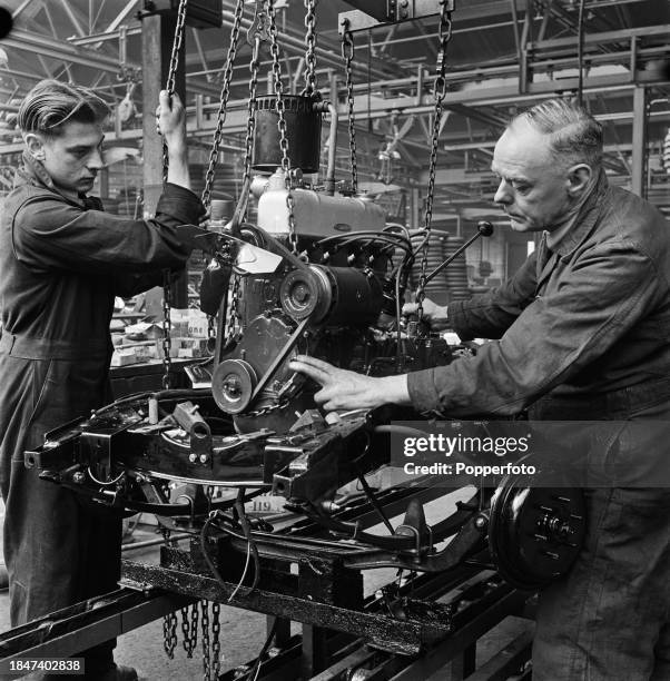Car workers and chassis assemblers lower a car engine into position on a Wolseley Eight car assembly line at a Wolseley Motors car factory, part of...