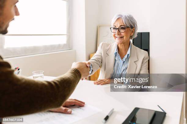 smiling senior woman handshaking hr male recruiter during job interview. rear view of young businessman shaking hand of joyful mature female after job interview. - job vacancy stock pictures, royalty-free photos & images
