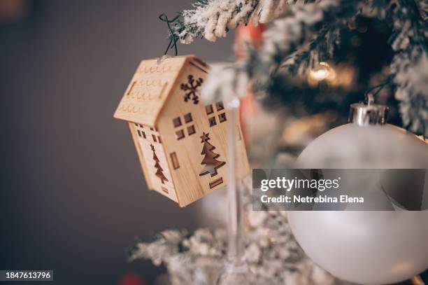 a toy wooden house is hanging on a christmas tree, glass balls and a garland. construction, moving to a new house, mortgage, rental and purchase of real estate. copy space - homeowners decorate their houses for christmas stockfoto's en -beelden