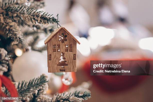 a toy wooden house is hanging on a christmas tree with balloons and a garland. construction, design, project, moving to a new house, mortgage, rental and purchase of real estate. copy space - homeowners decorate their houses for christmas stockfoto's en -beelden