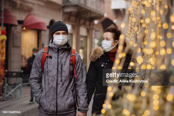 couple in medical masks in time of virus pandemic, walking along street - coronavirus ward stock pictures, royalty-free photos & images
