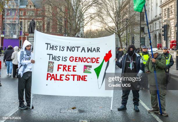 London, UK, Dec 9 2023, Masked pro-Palestinian protesters hold a banner "this is not a war. This is Genocide" in Parliament Square at a demonstration...