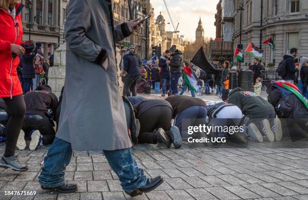 London, UK, Dec 9 2023, A man walks past a group of Muslim men praying in Trafalgar Square near Big Ben at a pro-Palestinian demonstration calling...