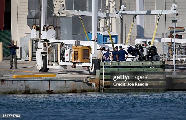 United States Coast Guard investigators look at a boat suspended on a boat lift at the United States Coast Guard Sector Station Miami after it...