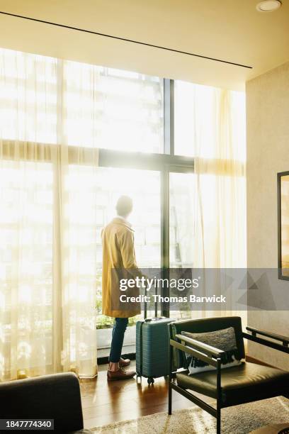 wide shot businessman looking out window of hotel during business trip - luxury hotel room stock pictures, royalty-free photos & images