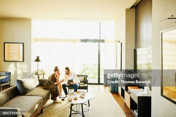 wide shot couple discussing information on smart phone in hotel suite - luxury hotel room stock pictures, royalty-free photos & images