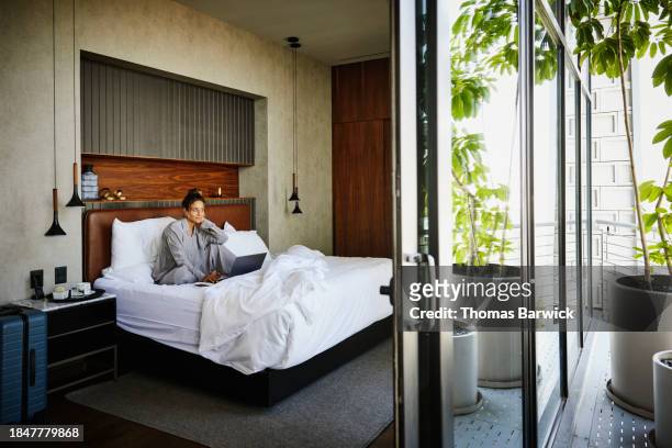 wide shot woman in bed working on laptop in hotel during business trip - luxury pyjamas stock pictures, royalty-free photos & images