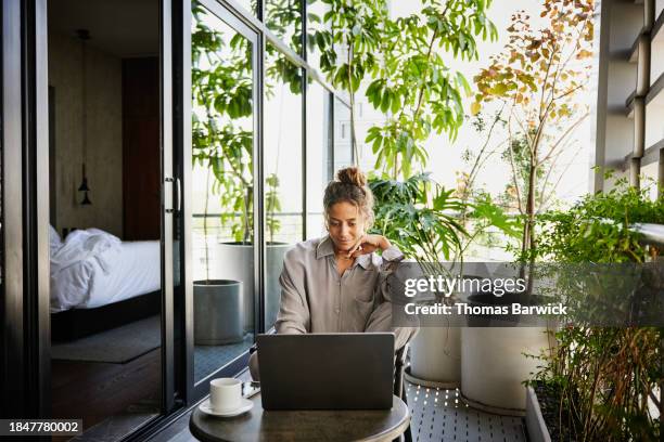 medium wide shot woman working on laptop on deck of hotel suite - luxury pyjamas stock pictures, royalty-free photos & images