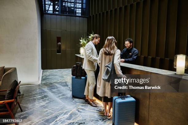 wide shot couple being assisted with check in at hotel front desk - plano geral imagens e fotografias de stock