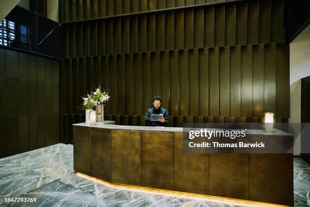 wide shot hotel manager working on digital tablet at hotel reception - hotel occupation stock pictures, royalty-free photos & images