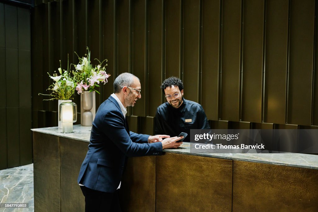 Wide shot hotel manager helping businessman at hotel front desk