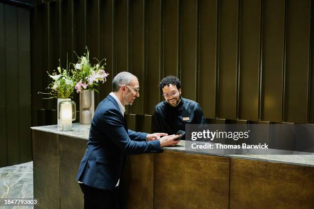 wide shot hotel manager helping businessman at hotel front desk - hotel stock-fotos und bilder