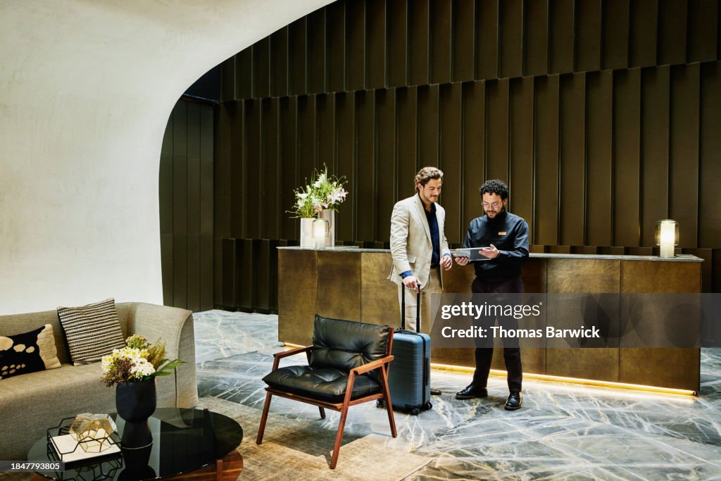 Wide shot manager checking businessman into hotel using digital tablet