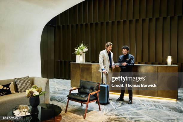 wide shot manager checking businessman into hotel using digital tablet - business class imagens e fotografias de stock