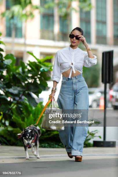 Heart Evangelista wears sunglasses, a golden watch, a white cropped shirt, a golden bracelets, high waist blue denim cuffed wide-leg jeans / pants, a...