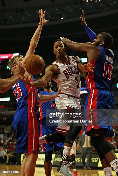 Derrick Rose of the Chicago Bulls passes between Kyle Singler and Greg Monroe of the Detroit Pistons during a preseason game at the United Center on...