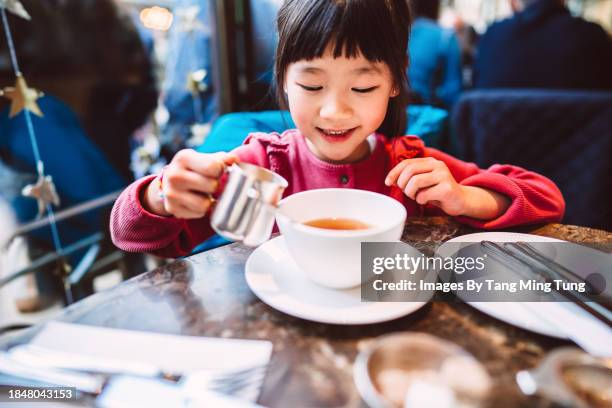 lovely cheerful girl pouring milk into a cup of hot tea while enjoying traditional afternoon in a restaurant - tea shop stock pictures, royalty-free photos & images