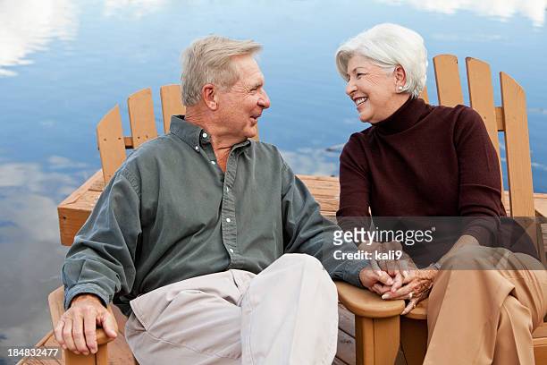 happy senior couple sitting by water - adirondack chair closeup stock pictures, royalty-free photos & images