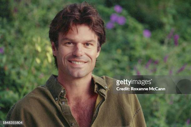 Harry Hamlin smiles for the camera wearing a collared shirt in his garden with puple and yellow flowers behind him in 1994 in Beverly Hills,...