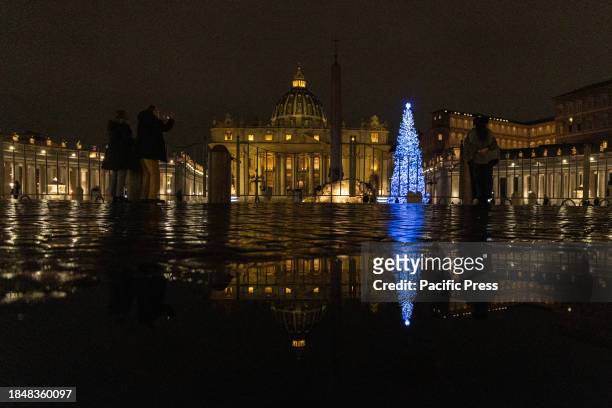 View of St. Peter's Square with the Christmas Tree and the Nativity scene reflected in a puddle.