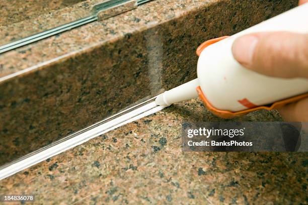 caulk gun applying silicone to granite sink backsplash - caulk stockfoto's en -beelden