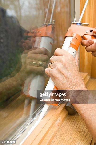 hands applying weather seal caulk to window frame - caulking stockfoto's en -beelden