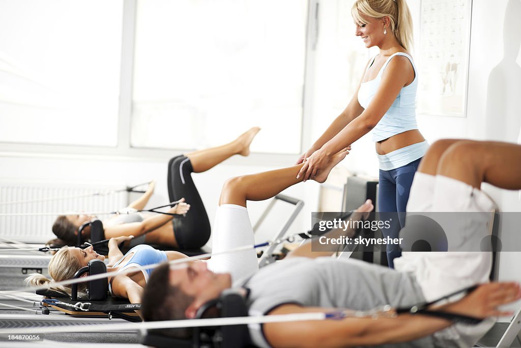 Coach assisiting the girl exercising on Pilates machine.