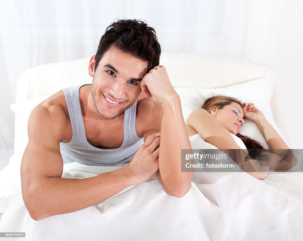 Smiling man in bed with beautiful sleepy woman