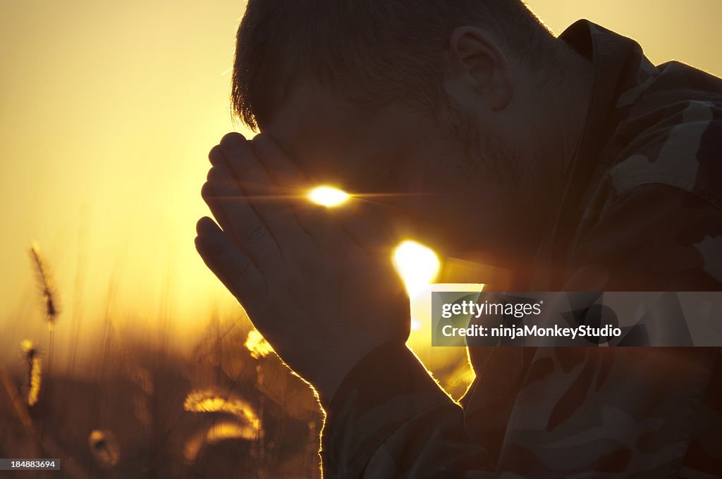 Soldado orar fora em campo ao pôr do sol