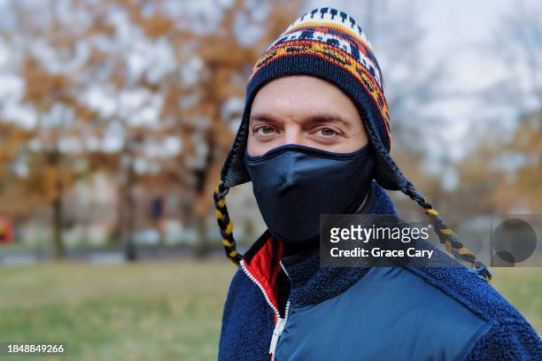 portrait of man wearing a colorful knit hat and protective face mask while outdoors on a chilly day - coronavirus winter stock-fotos und bilder