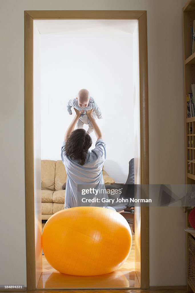 Mum balances on yoga ball holding baby up in hands