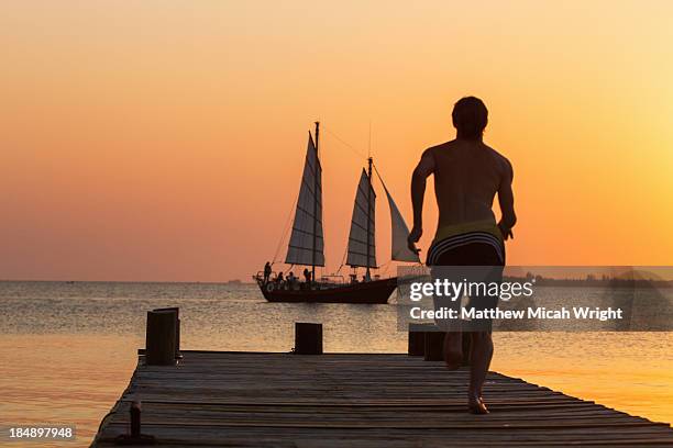 waterplay off a waterfront dock at sunset. - utila honduras stock pictures, royalty-free photos & images