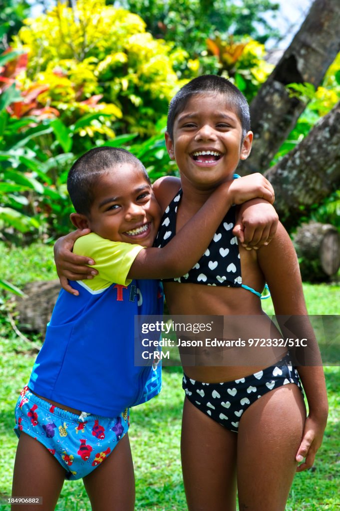 A brother and sister laughing and playing in a tropical garden.